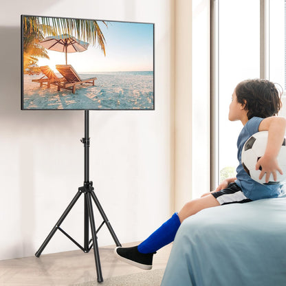 The black tripod display stand supporting a television in a bright bedroom setting