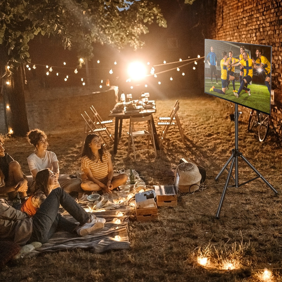 The black tripod display stand holding a television screen during an outdoor evening gathering
