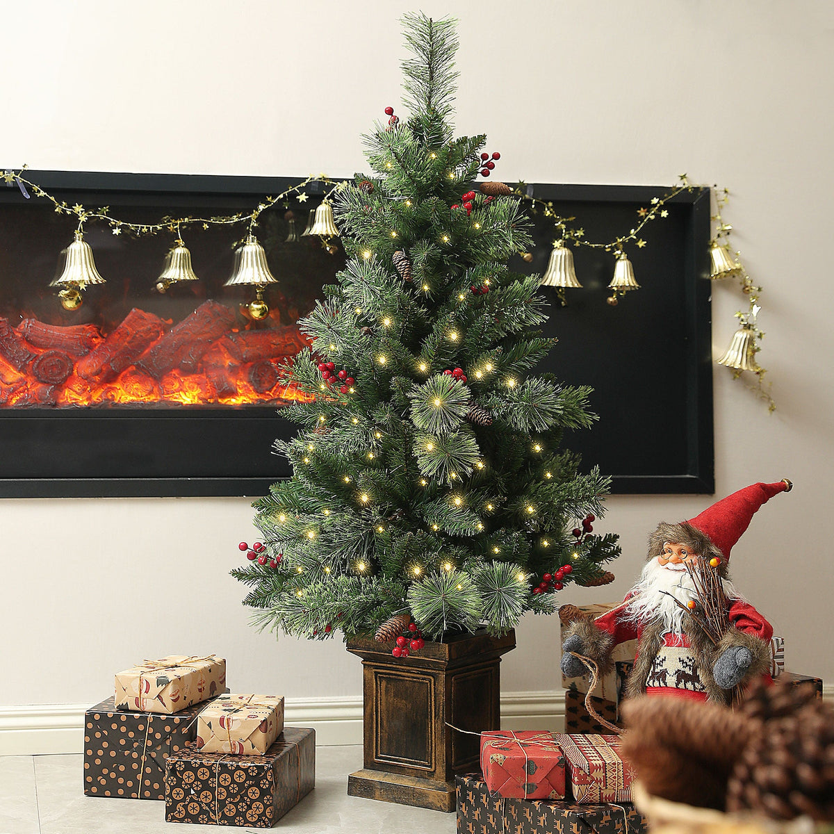 The pre lit Christmas tree placed in a living room next to a fireplace with gifts and decorations