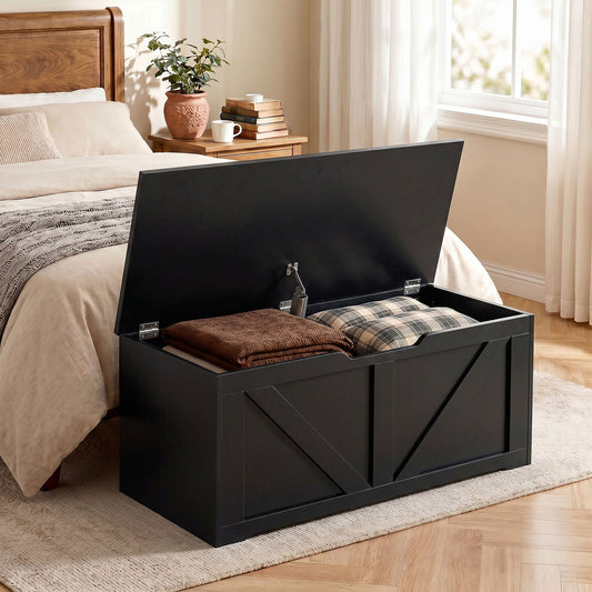 Black wood-effect storage box with lid open, placed at the end of a bed