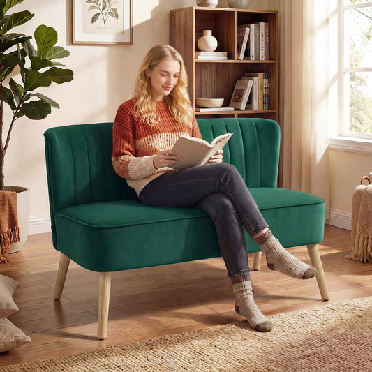 A woman sits reading a book on the dark green upholstered two-seater sofa in a living room setting