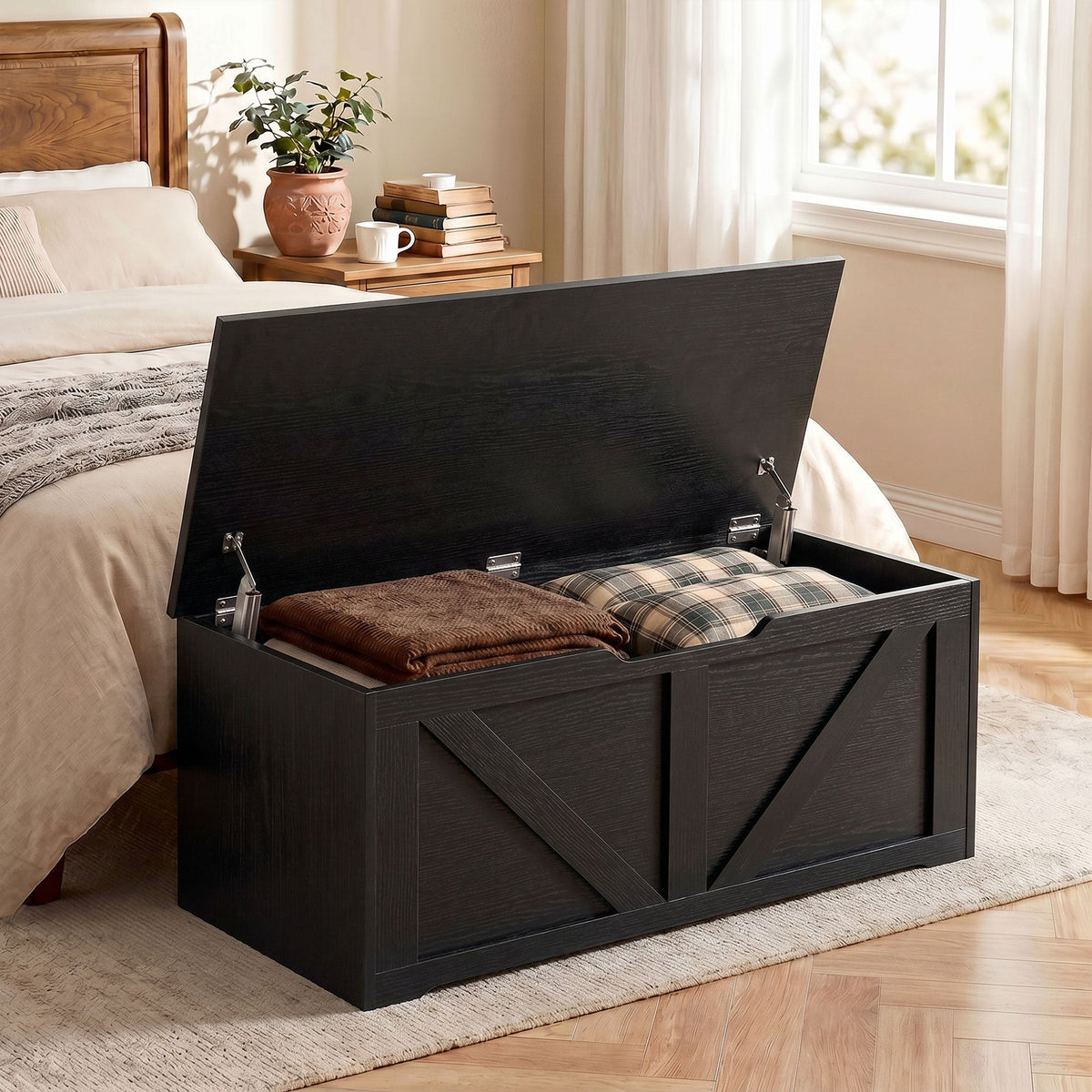 Black wood-effect storage box with lid open, placed at the foot of a bed with blankets inside