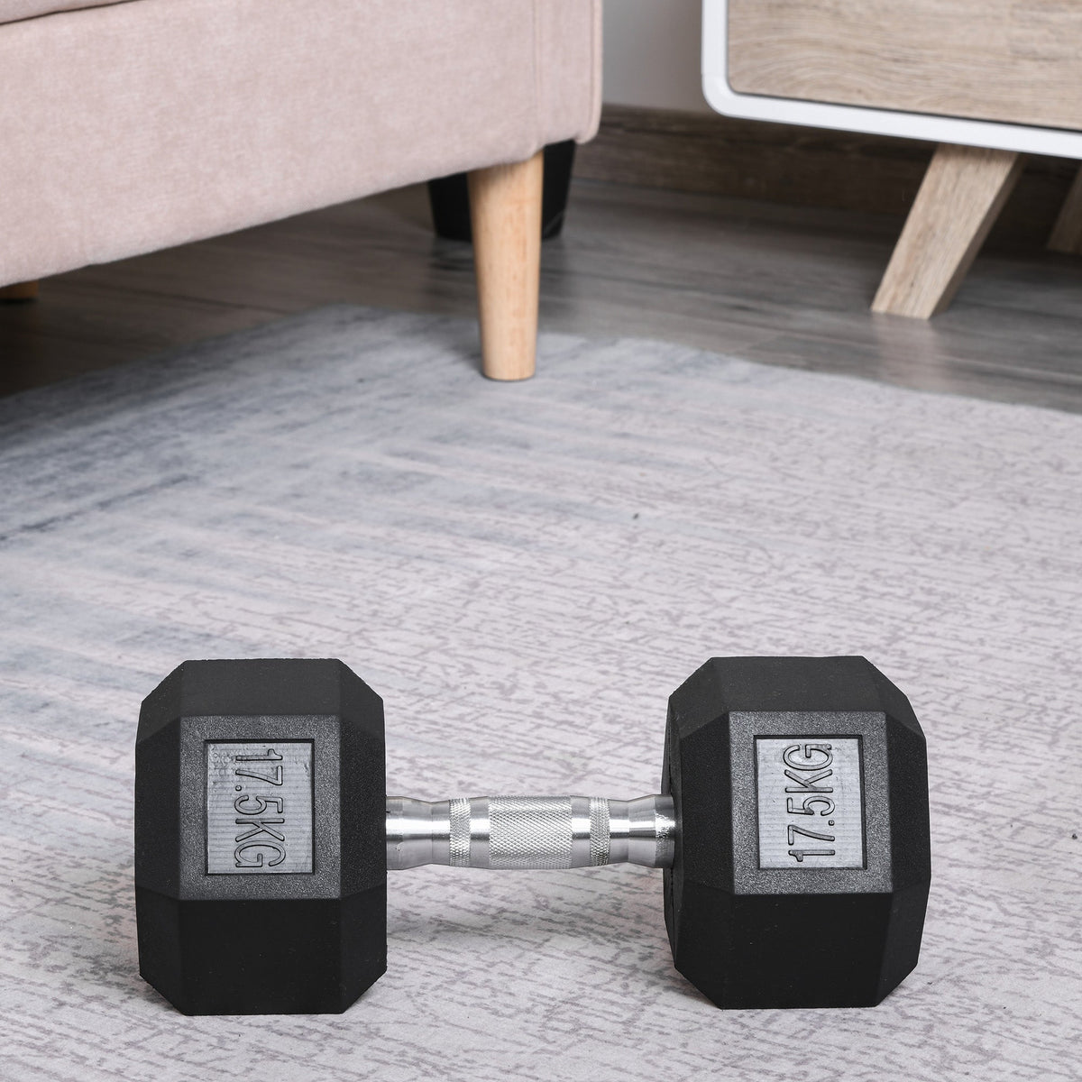 The rubber dumbbell resting on a grey carpeted floor in a home living room setting