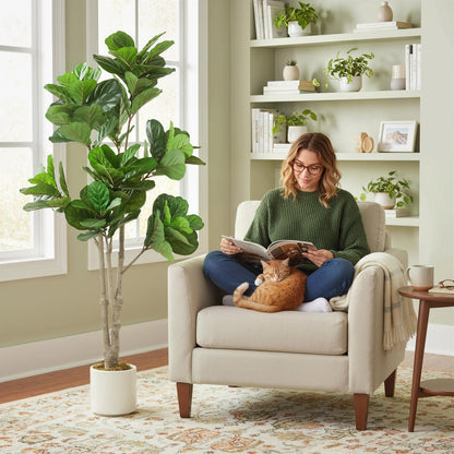 Woman reading a magazine next to the artificial fiddle leaf fig tree in a living room