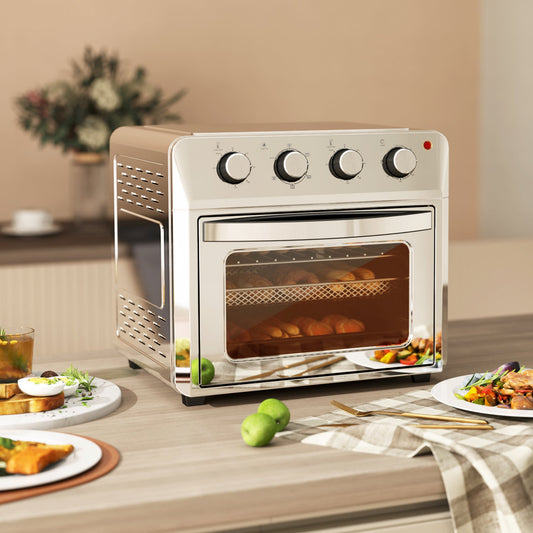 The mini oven on a kitchen counter, with food items like toast, chicken wings, and pizza arranged around it