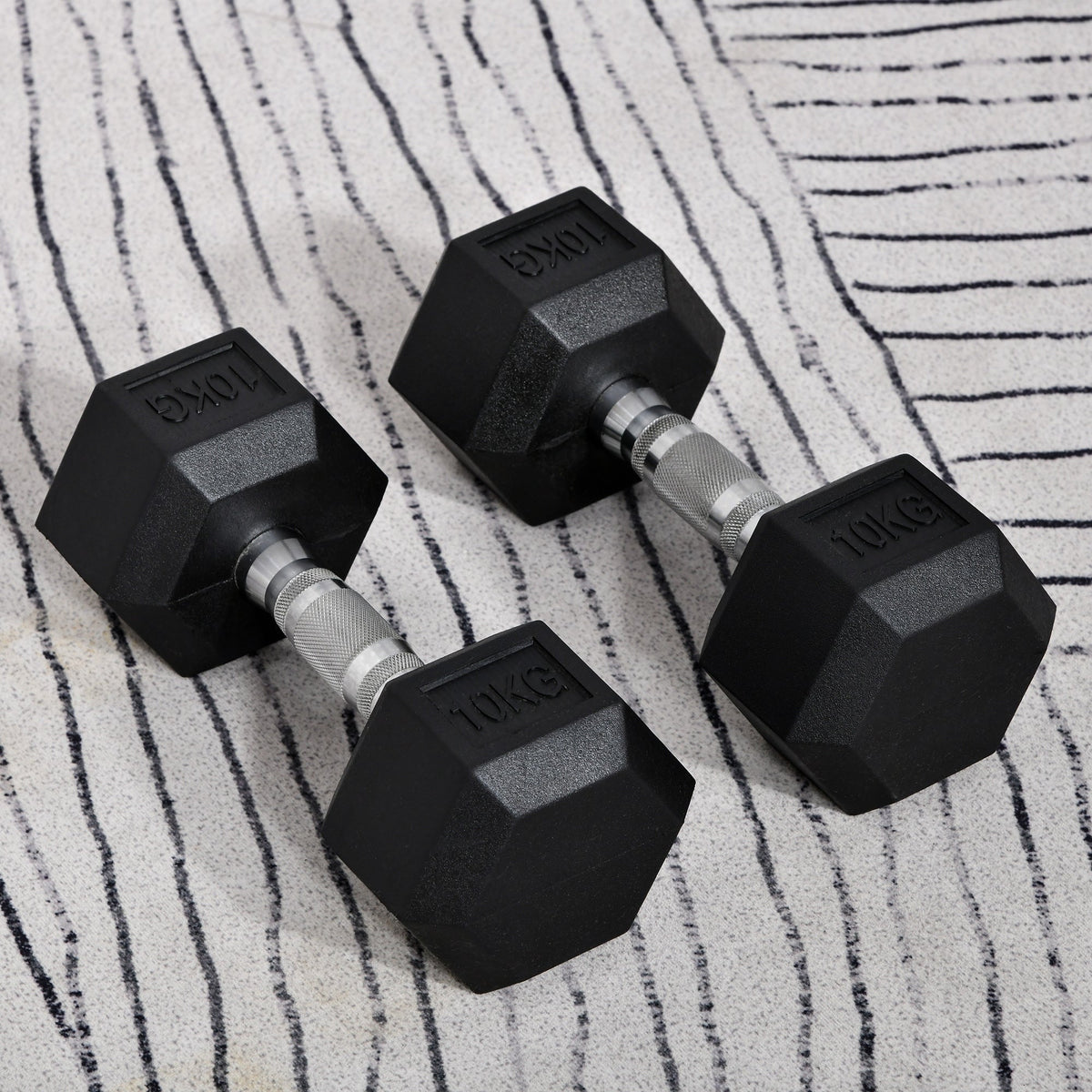 The pair of black rubber dumbbells resting on a textured grey and white rug