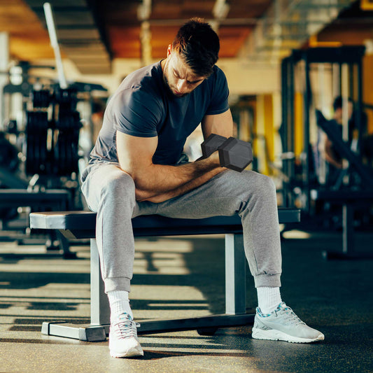 Man sitting on a bench in a gym, lifting a rubber hex dumbbell for a bicep curl