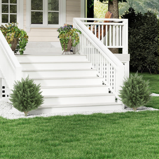 Two artificial cypress trees flanking a white outdoor staircase with potted plants