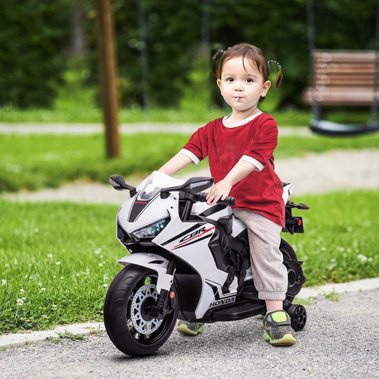 A toddler rides the white Honda licensed kids electric motorbike with training wheels on a paved path