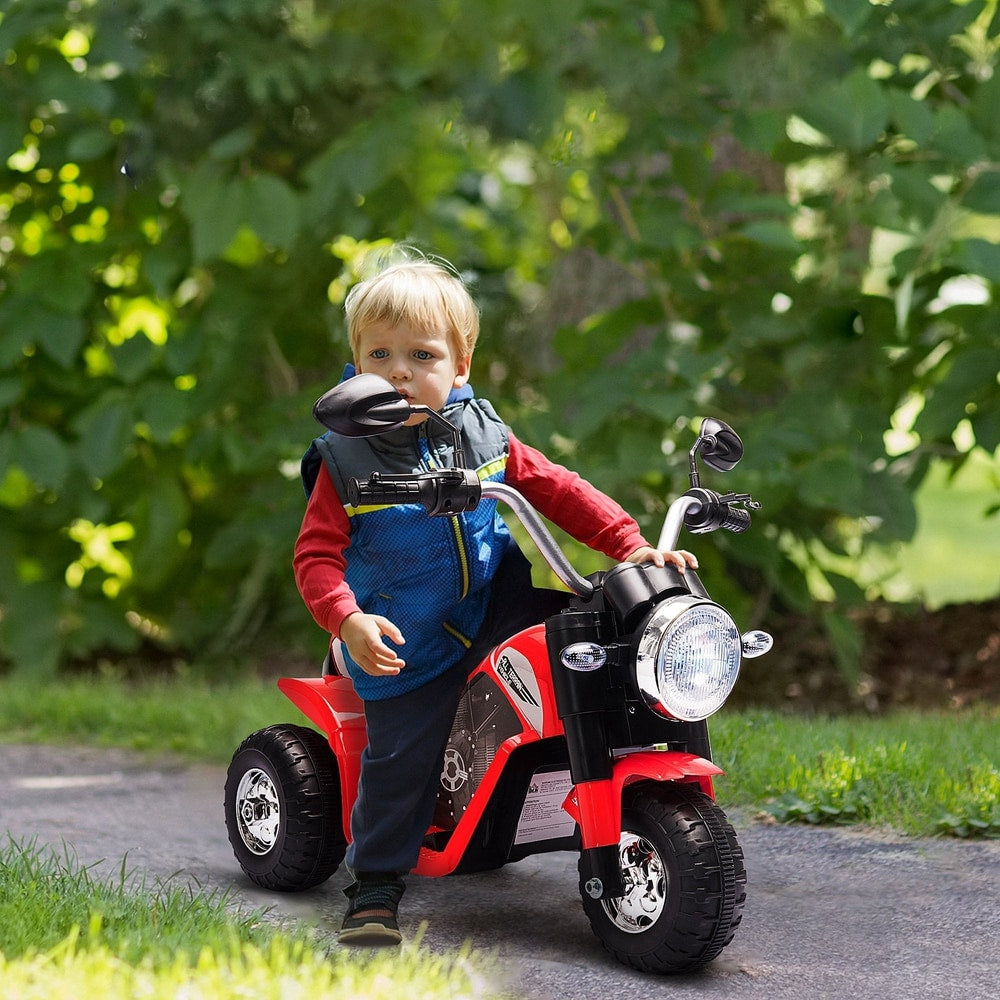 A young boy rides the red kids electric motorbike toy outdoors on a paved path