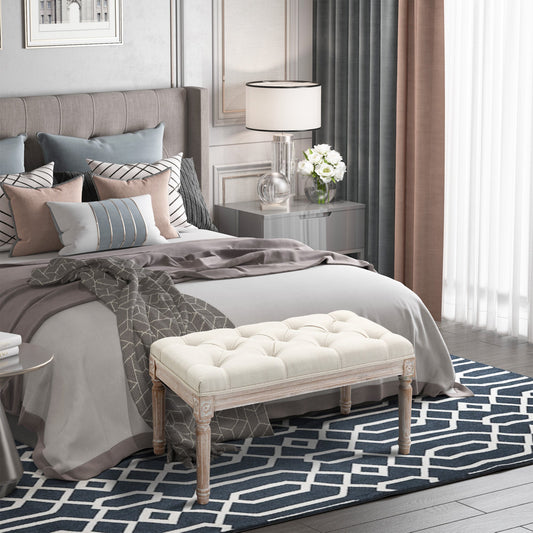 The cream white tufted bench is placed at the end of a bed in a bedroom setting