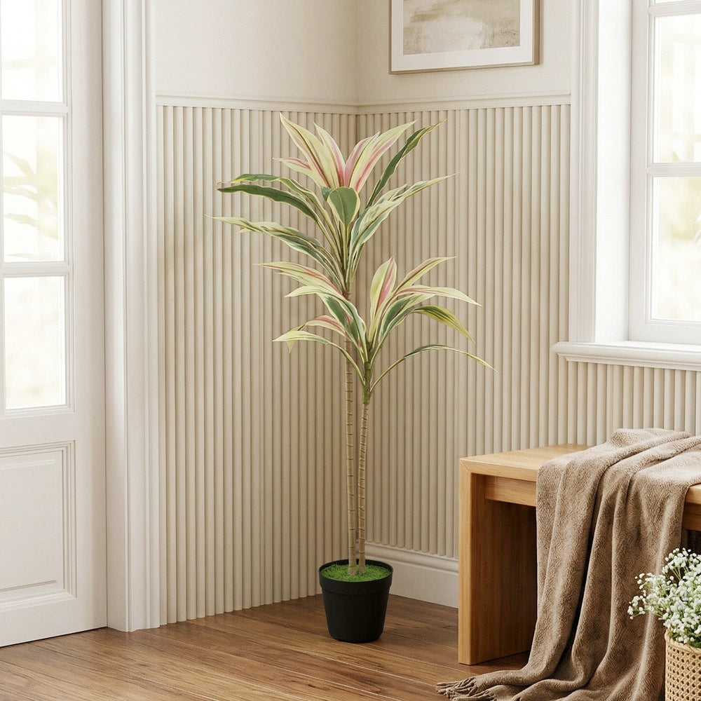 Artificial cordyline tree in a black pot placed in a living room next to a wooden bench