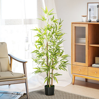 The artificial bamboo plant is shown in a domestic setting next to wooden furniture