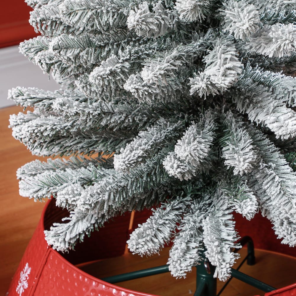 Close up of the snowy branches and the red tree skirt of the pencil Christmas tree