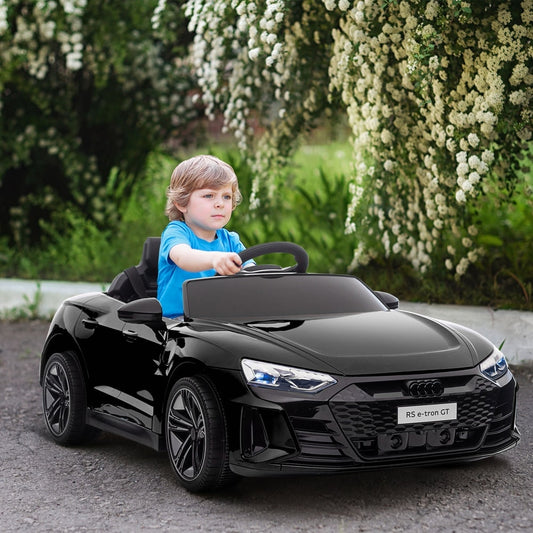 A young boy driving the black kids electric ride-on car on a paved path surrounded by greenery