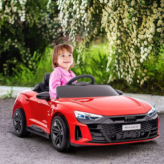 A young child sitting in the red kids electric ride-on car parked on a path near white flowers