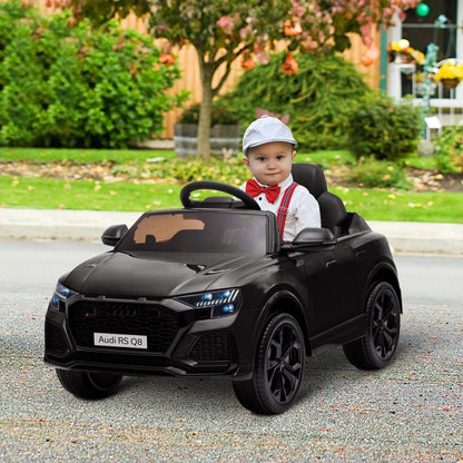 A young boy wearing a cap and bow tie sitting inside the black electric ride-on car outdoors