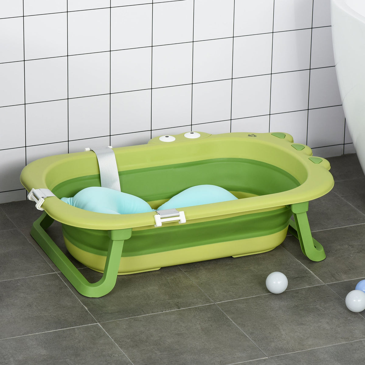 Green foldable baby bath tub with a blue cushion, set against a tiled wall