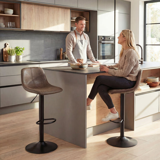 Two brown swivel bar stools placed at a kitchen island with a man and woman sitting nearby