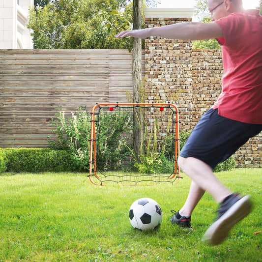 A man kicking a football towards the football rebounder net set up on grass