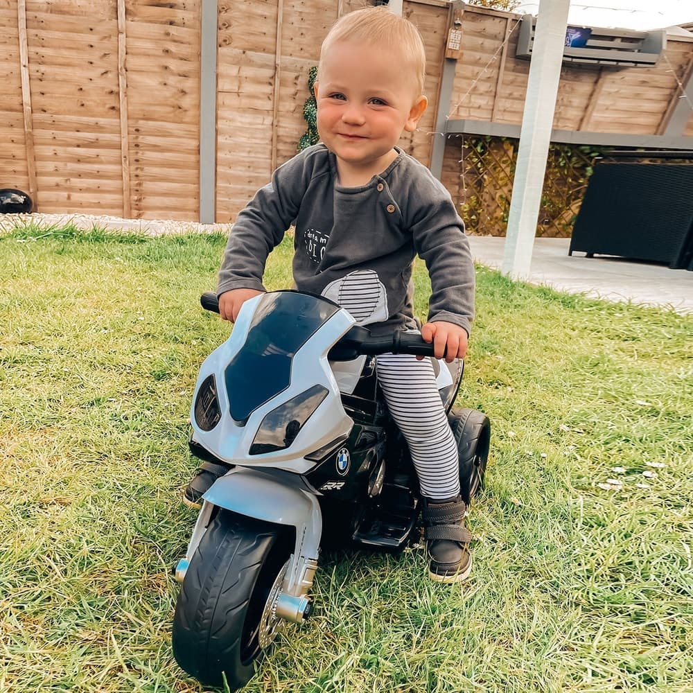 A young child sitting on the kids electric motorbike while playing on a grassy lawn