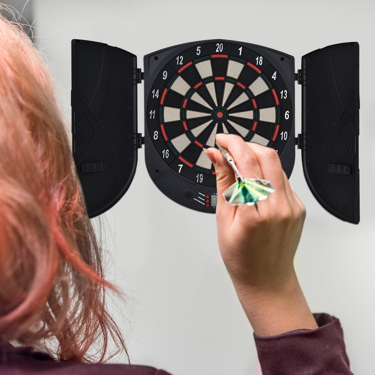 the electronic dartboard mounted on a wall being used by a person throwing a dart