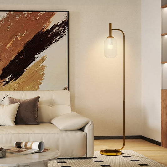 A modern gold floor lamp with a glass shade standing next to a sofa in a living room