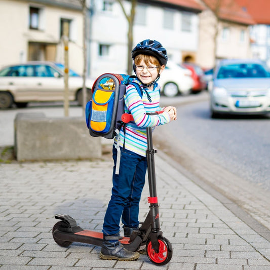 A young boy wearing a helmet and backpack riding the red and black electric scooter on a street