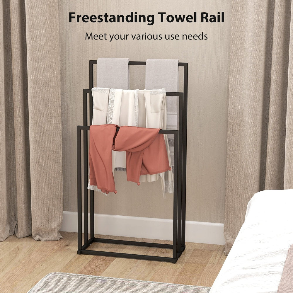 The black towel rail holder is shown in a bedroom with towels and clothes