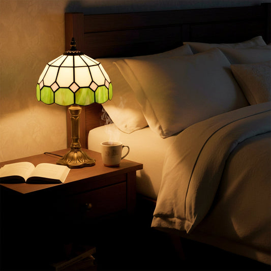 The table lamp is on a bedside table next to a bed with a book and mug