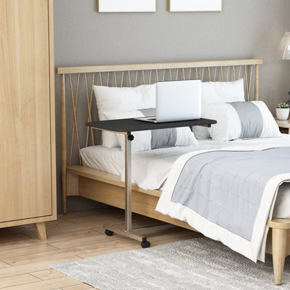 The side table positioned over a bed with a laptop placed on the black surface