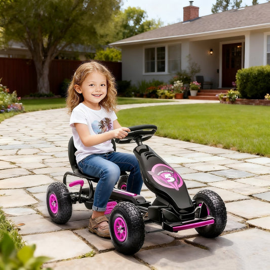 A young girl happily rides the pink pedal go kart on a paved driveway