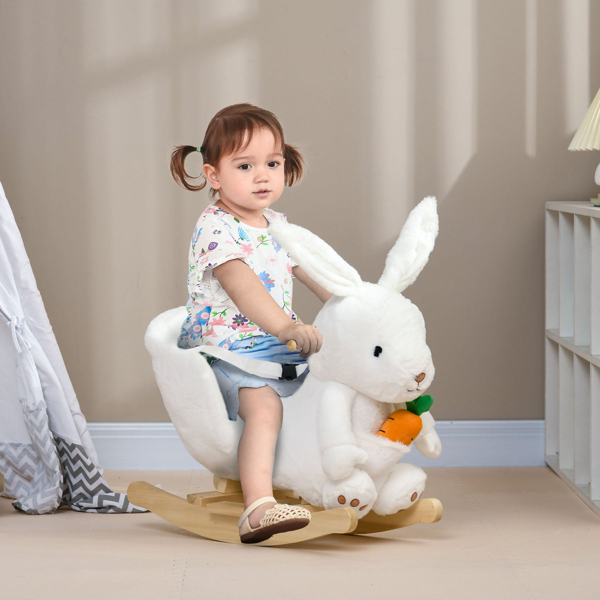 A toddler sitting on the white plush rocking rabbit animal in a nursery room