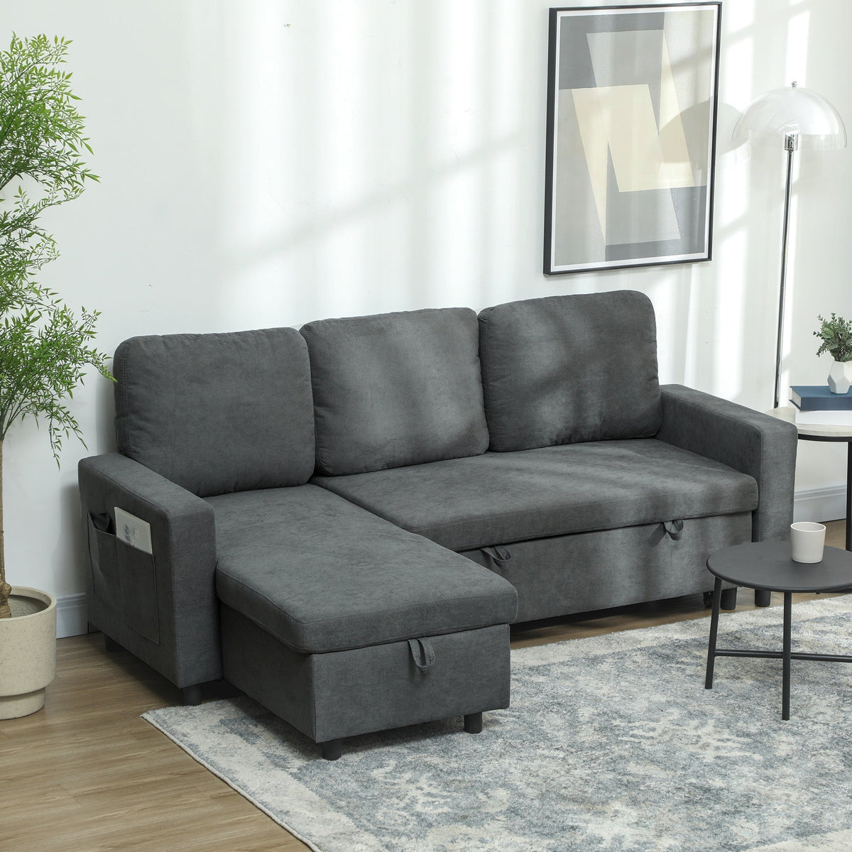 The charcoal grey sofa bed is set up in a living room with a plant and lamp