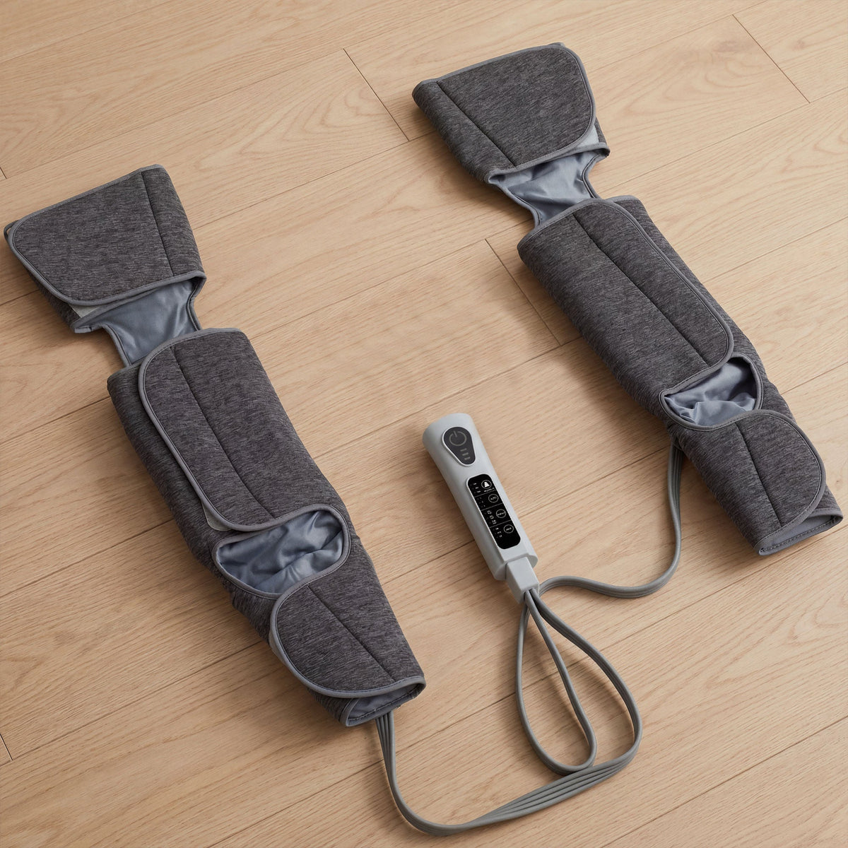 The grey fabric foot and calf compression machine with heat laid out flat on a wooden floor