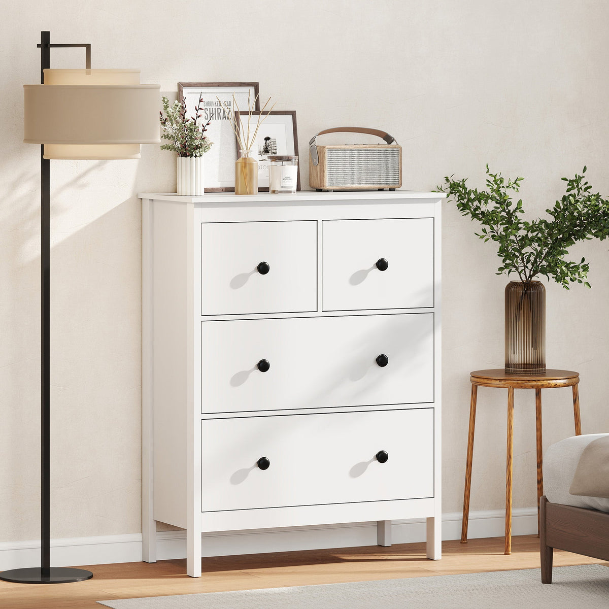 The white four-drawer dresser in a tidy bedroom setting next to a lamp and side table