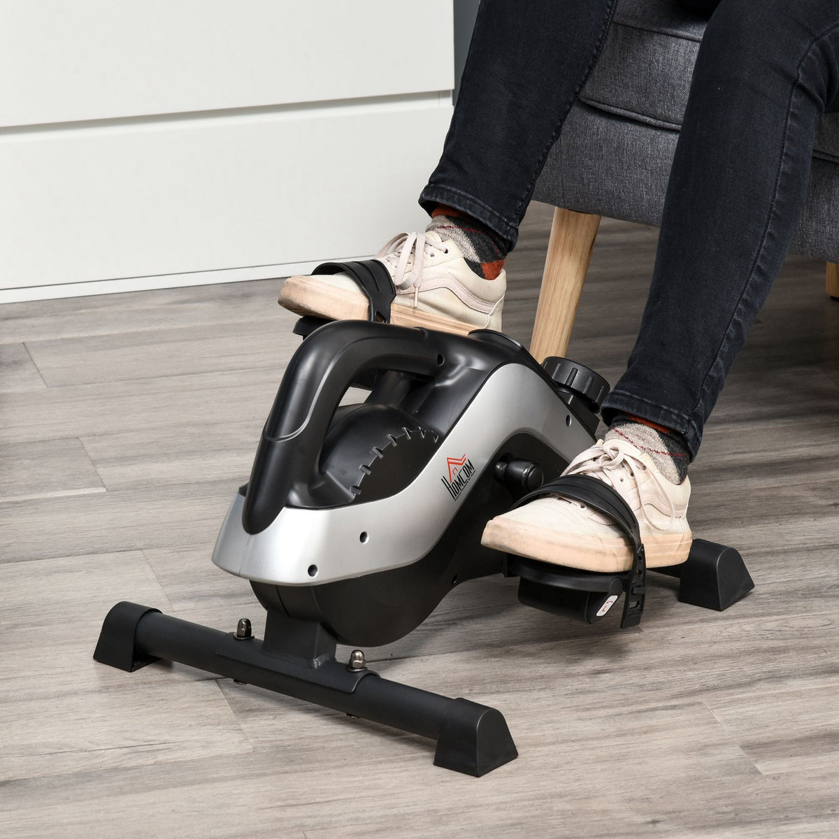A person using the mini exercise bike while sitting down, with feet on the pedals