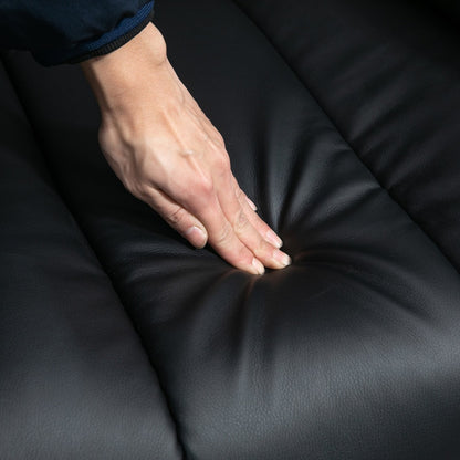 A hand presses into the soft padding of the black electric armchair's seat