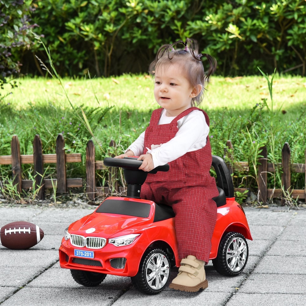A baby sits on the red ride-on car in a garden setting