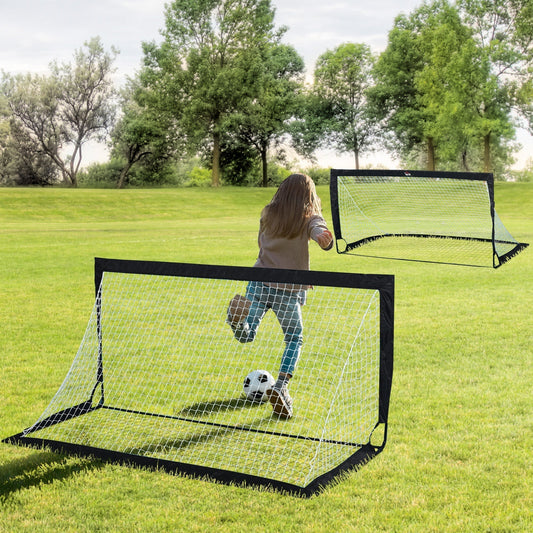 A girl kicks a football towards a small football goal net in a garden setting
