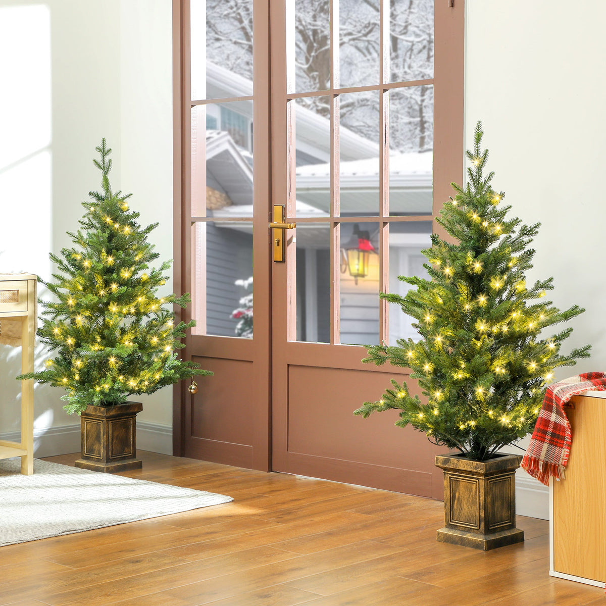 Two artificial Christmas trees with lights, placed in a hallway by a door