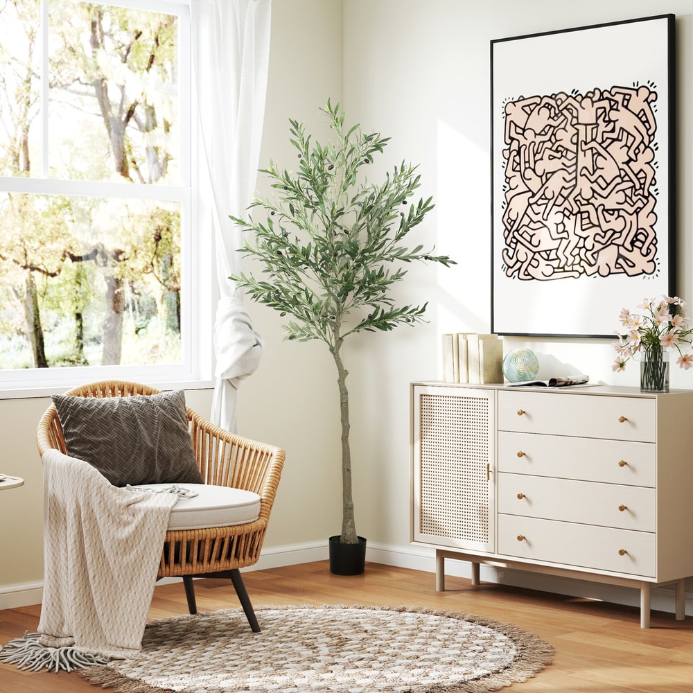 The artificial olive tree placed in a bright living room next to a rattan chair and a cabinet