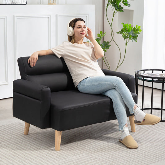A woman sits on the black faux leather two-seater sofa, wearing headphones and looking relaxed
