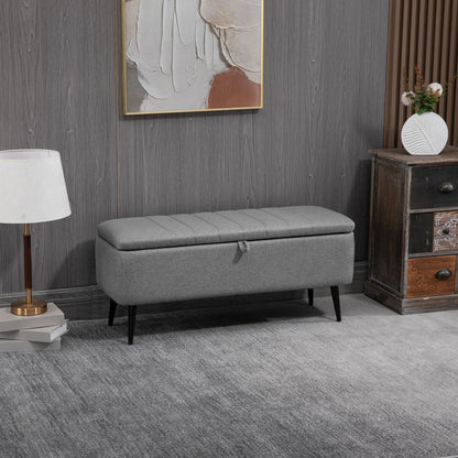 The grey storage bench in a living room setting, placed next to a cabinet and lamp