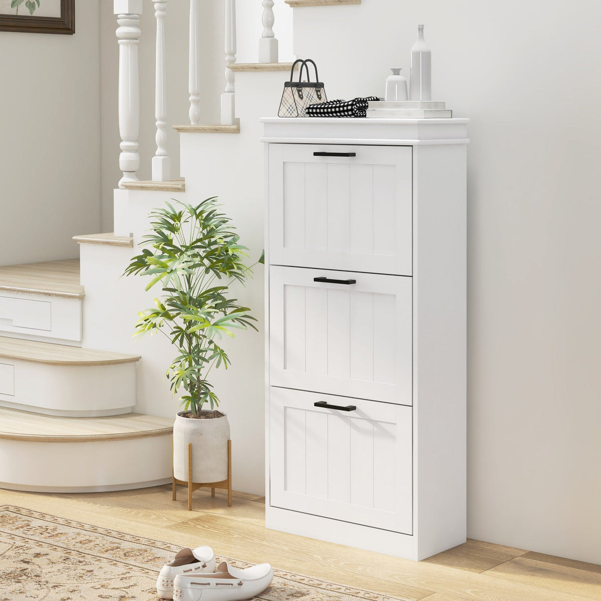 The white three-tier shoe storage cabinet placed in a hallway next to stairs with a plant and shoes