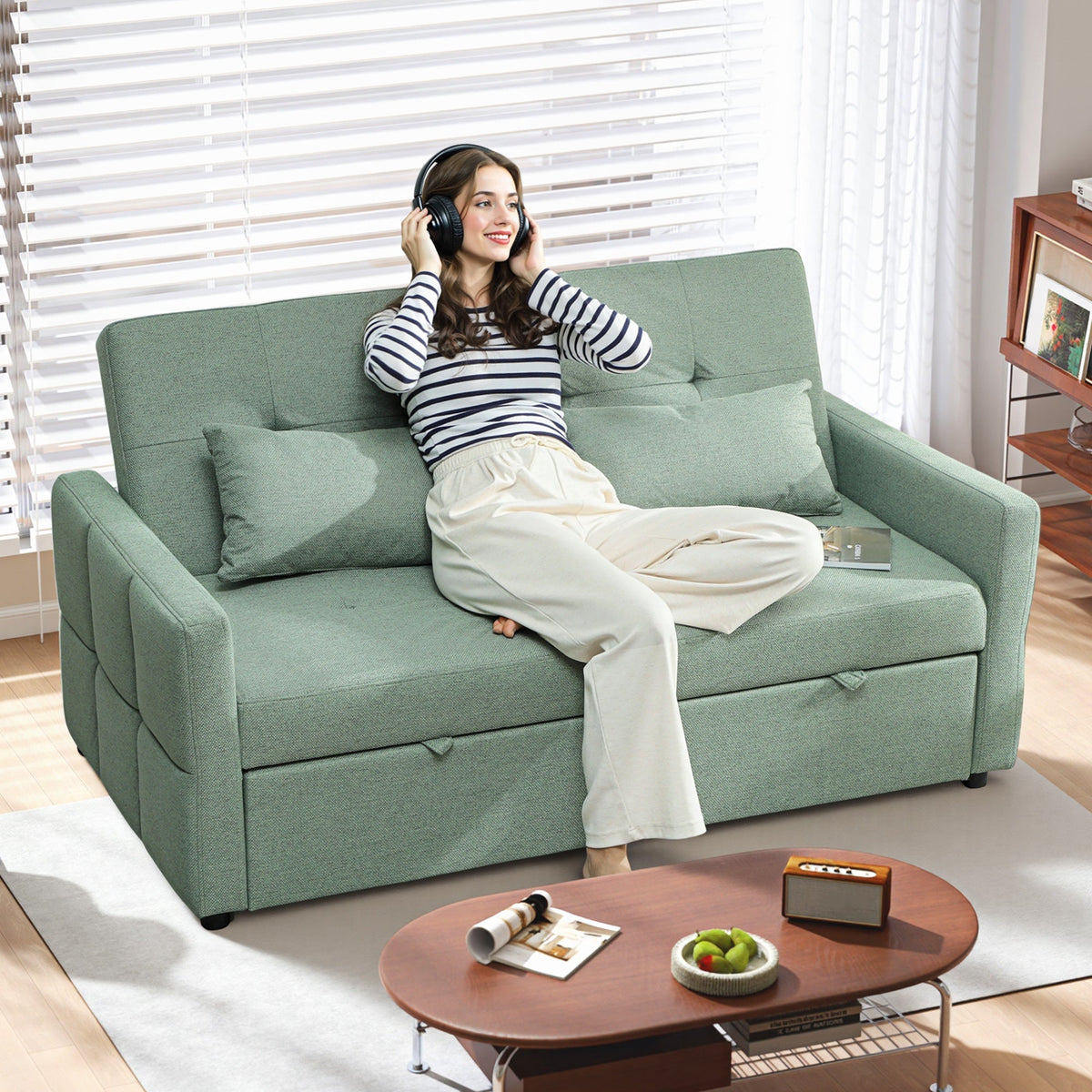 A woman wearing headphones sits on the green sofa bed in a living room
