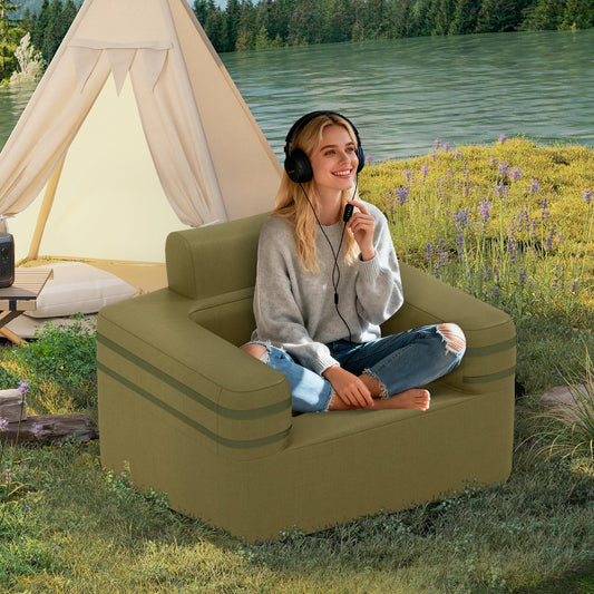 The camping furniture placed on grass by a lake with a woman sitting in it wearing headphones