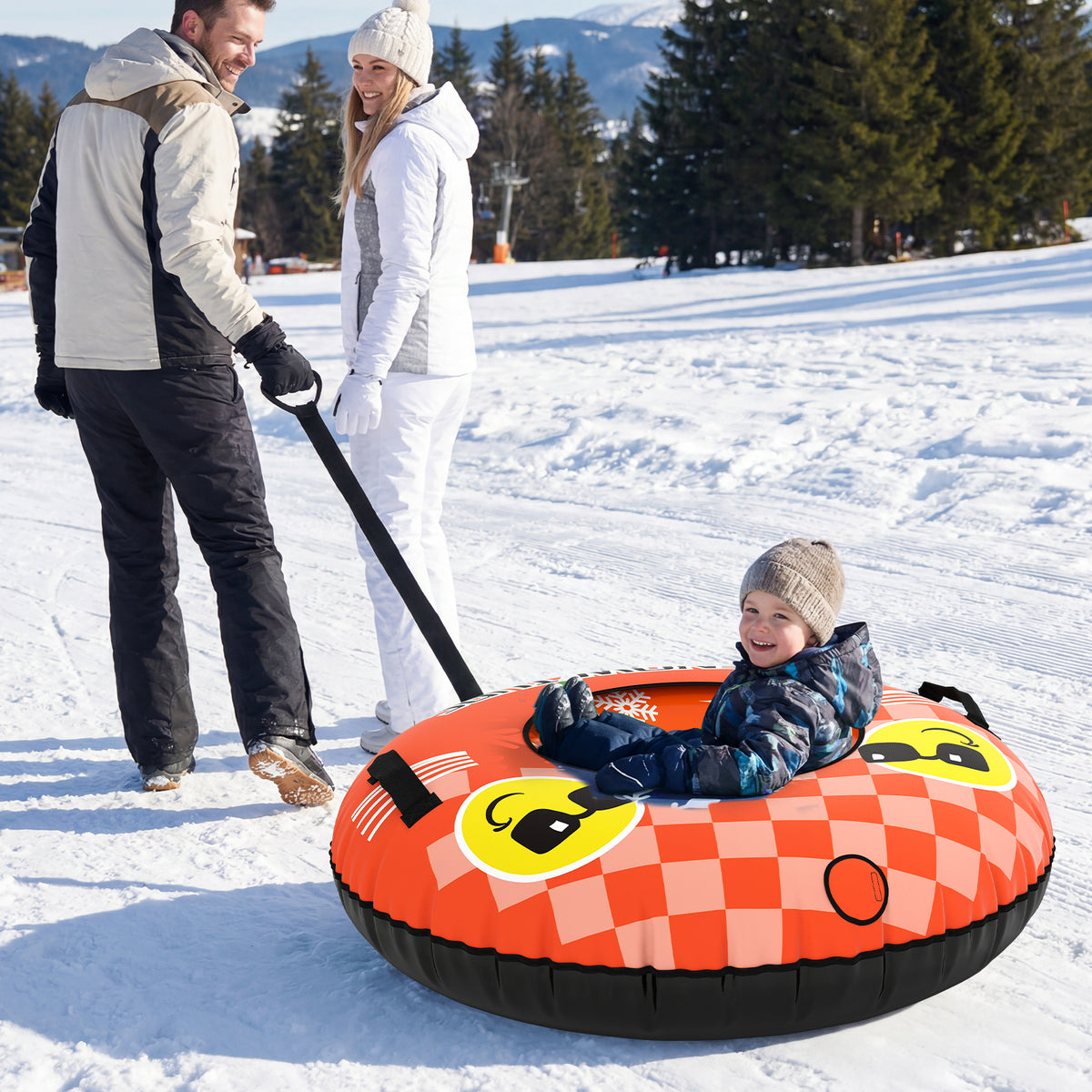 An orange inflatable snow tube with a smiling face design, being pulled by adults across snow