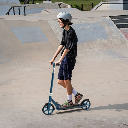 A teen wearing a helmet rides the blue kick scooter in a skate park