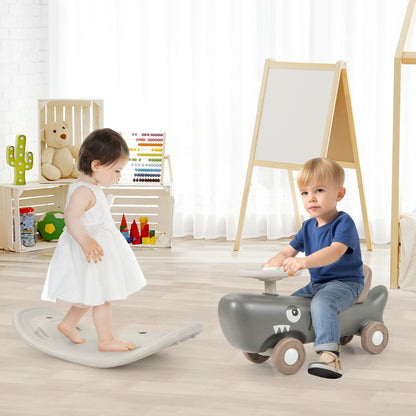 A toddler sits on the grey rocking horse and sliding car in a room